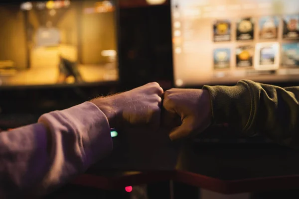 Two players touching fists over the desk in front of a bright screen just before play starts