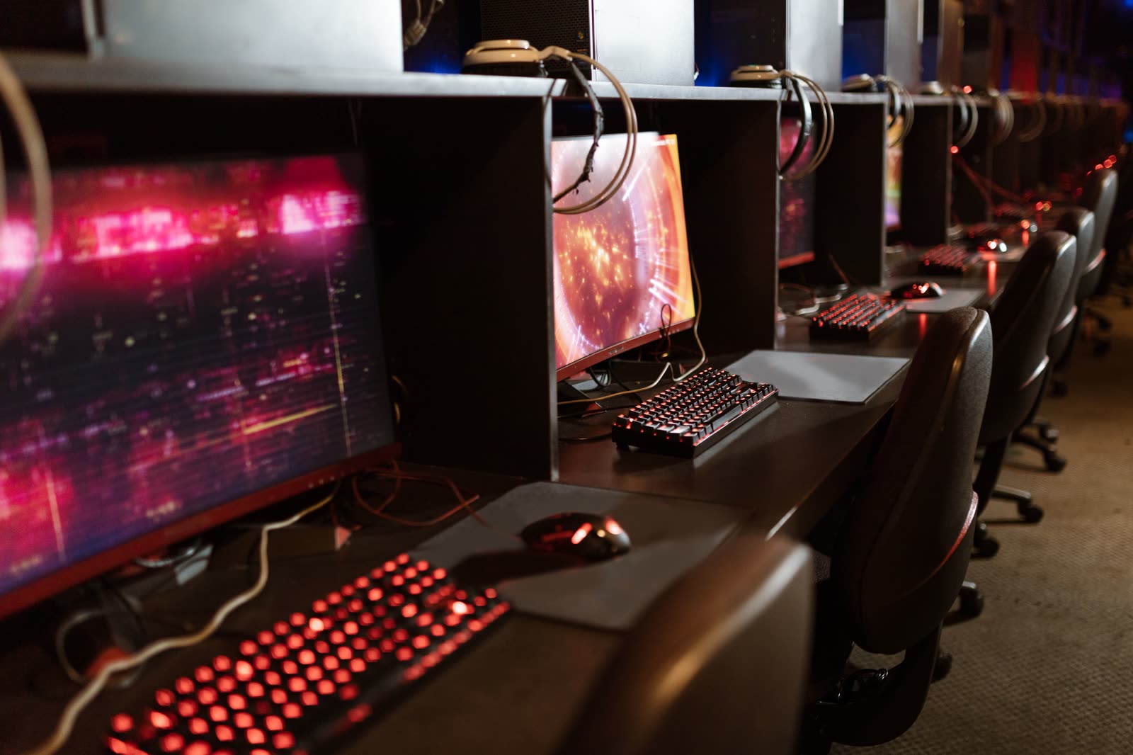 A long row of identical gaming stations receding into the dark, monitors and keyboards lit red down the aisle